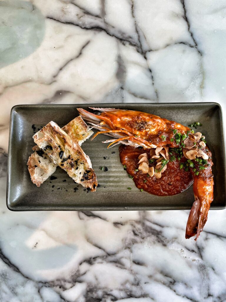 BBQ prawn on a plate served with bread and oil atop a homemade bacon XO sauce.